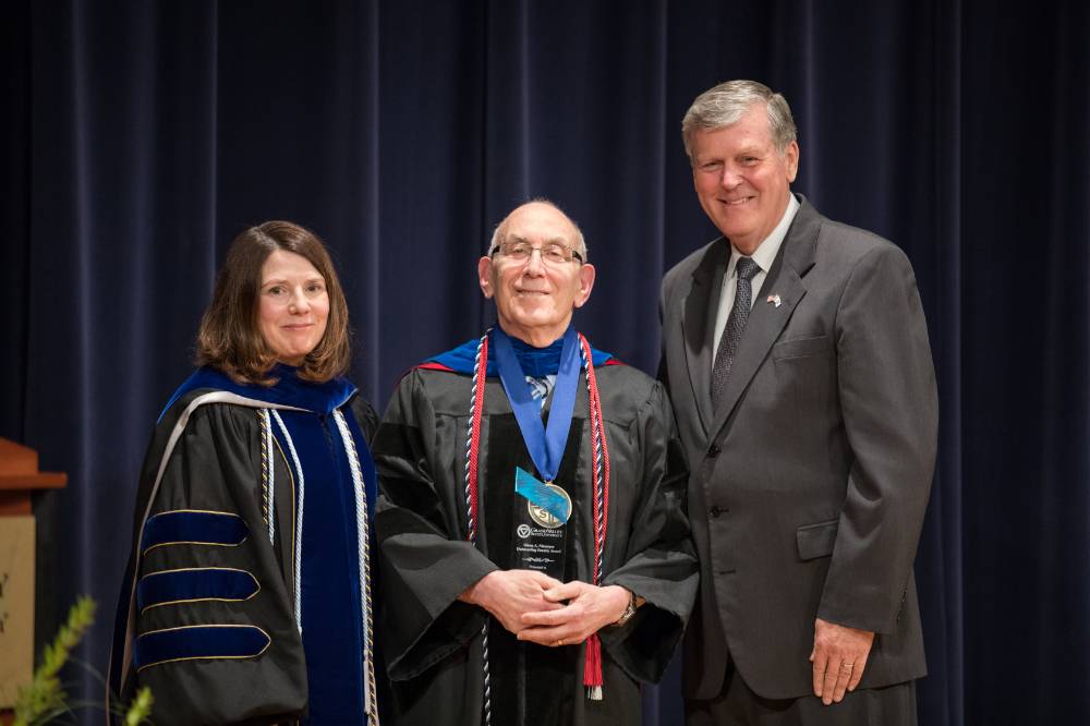 Provost, faculty member and President Emeritus Haas smile for a photo on stage.